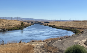 Irrigation canal stretching through dry hills with wind turbines on the distant ridgeline