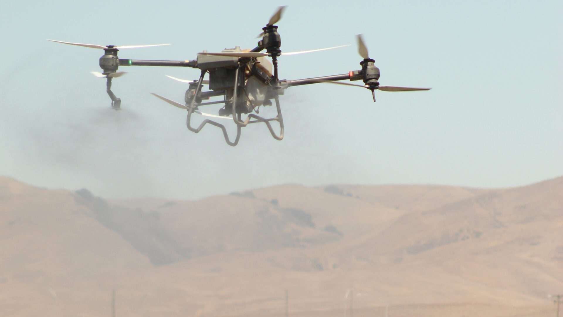 Agricultural spray drone flying low over a field with dry foothills in the background